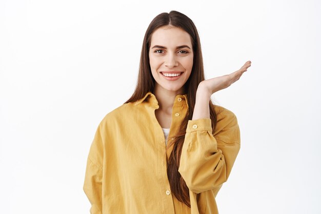 Immagine di bella donna con trucco naturale nudo e sorriso bianco, aprire metà del viso, allontanare la mano e guardare davanti, prima e dopo l'effetto, in piedi sul muro bianco