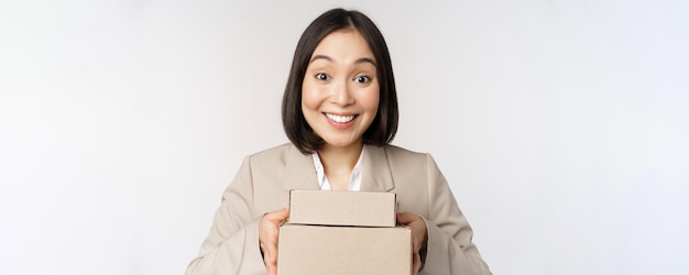 Immagine di donna d'affari commessa asiatica che dà scatole con ordine consegnare al cliente in piedi in tuta su sfondo bianco