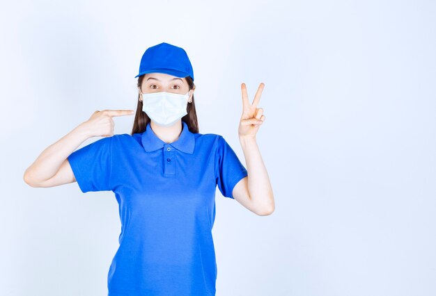 Immagine di donna in uniforme e maschera medica che mostra il segno della vittoria.