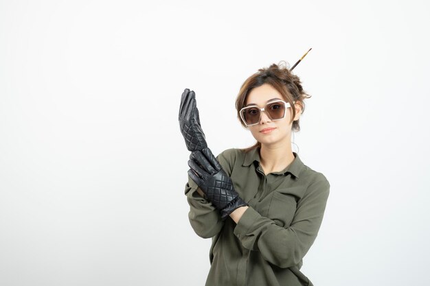 Immagine di giovane donna adorabile con gli occhiali e guanti neri in piedi. Foto di alta qualità