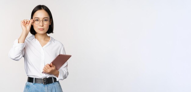 Immagine di giovane donna d'affari asiatica imprenditrice in bicchieri tenendo tablet e cercando professionale in bicchieri sfondo bianco