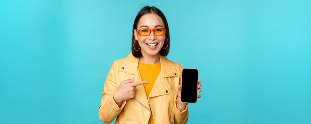 Immagine di giovane modello femminile asiatico alla moda in occhiali da sole alla moda che mostra l'applicazione dello schermo del telefono cellulare