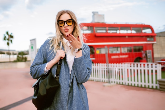 Immagine di moda all'aperto di giovane donna alla moda che propone alla via di Londra, vestito elegante di affari casuali, invio di bacio e guardando sulla fotocamera, tempo di mezza stagione autunno primavera, colori tonica.