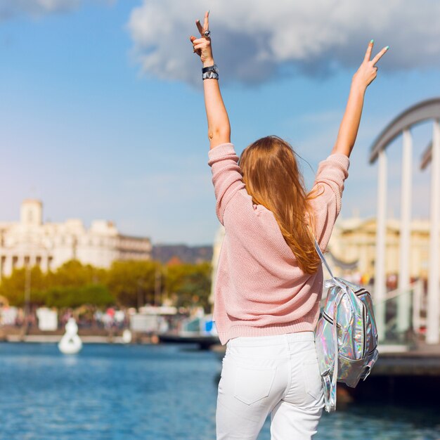 Immagine di stile di vita della ragazza dei pantaloni a vita bassa in attrezzatura pastello casuale di primavera, gioielli d'avanguardia, labbra rosse che godono delle vacanze a Barcellona.