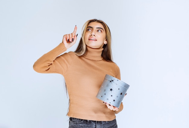 Immagine di un modello di giovane donna in maglione marrone con una confezione regalo rivolta verso l'alto.