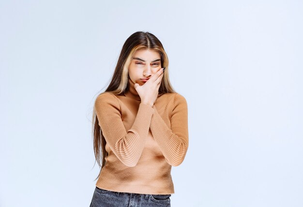 Immagine di un modello di giovane donna in maglione marrone in piedi e tenendo la guancia.