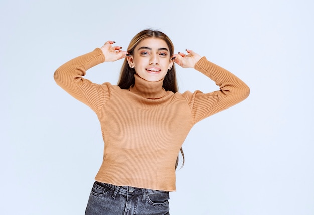 Immagine di un modello di giovane donna in maglione marrone in piedi e tenendo le orecchie.