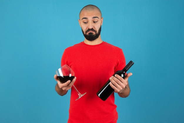 Immagine di un modello di giovane uomo in maglietta rossa che tiene in mano una bottiglia di vino con un bicchiere.