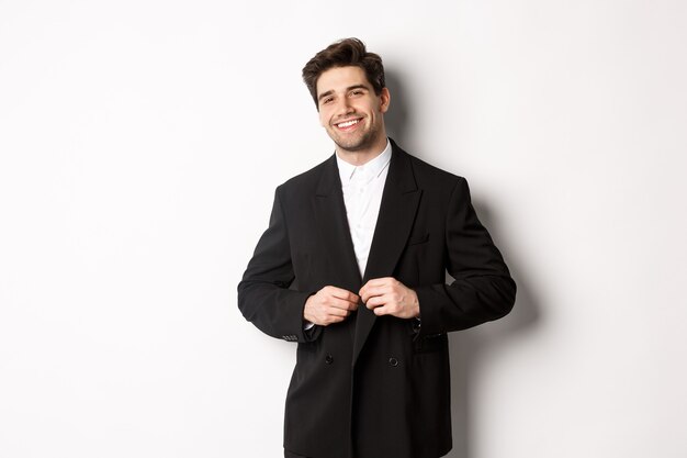 Immagine di un uomo d'affari bello e fiducioso con barba, giacca abbottonata e sorridente, in piedi su sfondo bianco