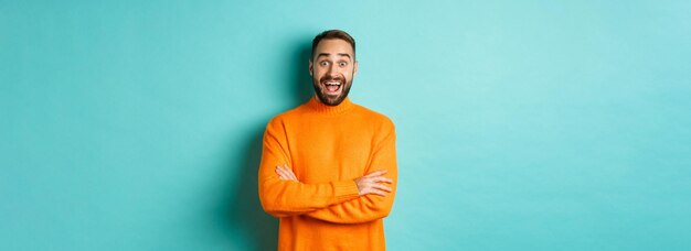 Immagine di un uomo felice e sorpreso che reagisce alle notizie guardando stupito in piedi in un maglione arancione contro