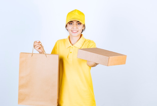 Immagine di una bella donna in uniforme gialla che tiene in mano una scatola e una borsa di carta artigianale in bianco marrone.