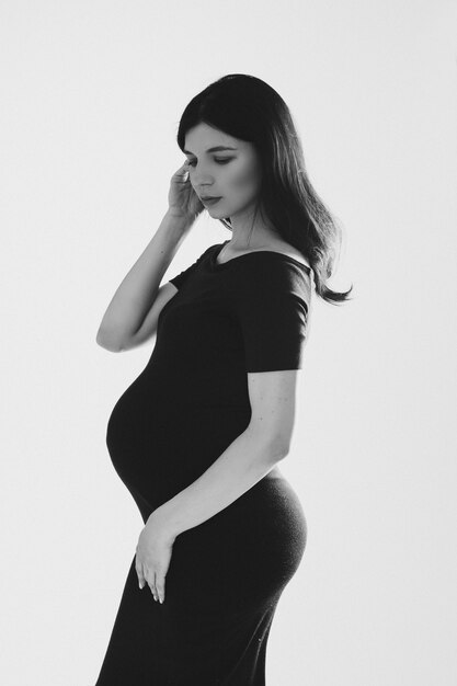 Immagine di una bella donna incinta caucasica che si tocca i capelli lunghi, foto in bianco e nero isolata su sfondo bianco