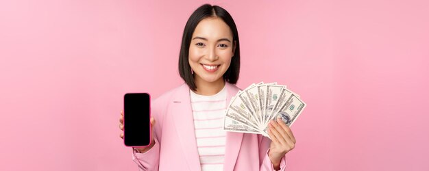 Immagine di una donna d'affari coreana di successo che mostra i dollari di denaro e l'interfaccia dello schermo dell'app per smartphone