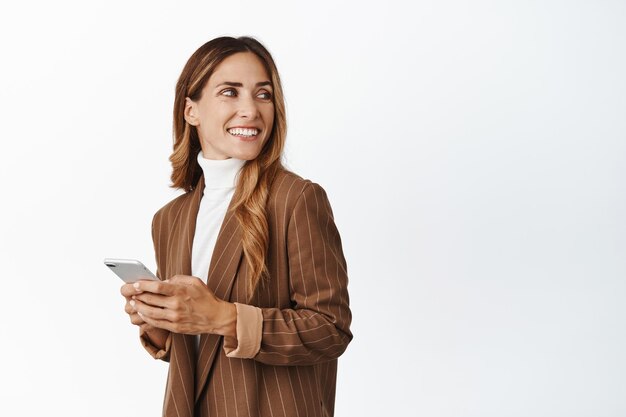 Immagine di una donna di mezza età che tiene il telefono cellulare guardando da parte il nome del prodotto dell'azienda dello spazio di copia in piedi su uno sfondo bianco