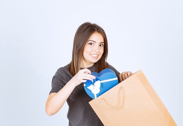 Immagine di una donna sorridente che mette un regalo a forma di cuore in un sacchetto di carta.