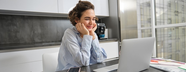 Immagine di una donna sorridente che studia al telecomando guardando il portatile mentre è seduta a casa a guardare il webinar