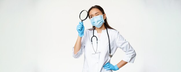 Immagine di una dottoressa asiatica con lente d'ingrandimento che indossa una maschera medica e guanti di gomma