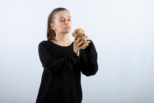 Immagine di una giovane modella in piedi che beve da una tazza di caffè