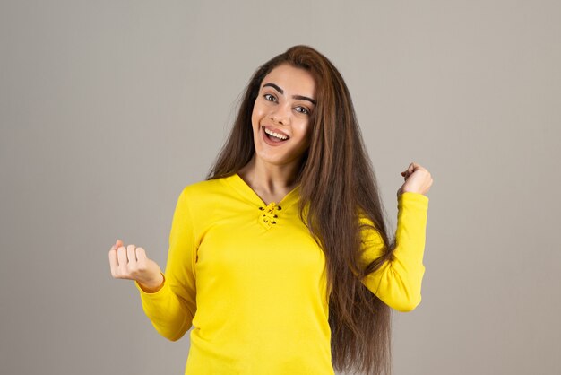 Immagine di una giovane ragazza in giallo in posa sul muro grigio.