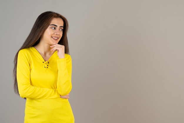 Immagine di una giovane ragazza in top giallo in piedi e in posa sul muro grigio.
