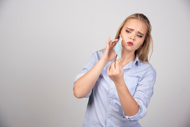 Immagine di una graziosa modella in piedi che si toglie una maschera medica