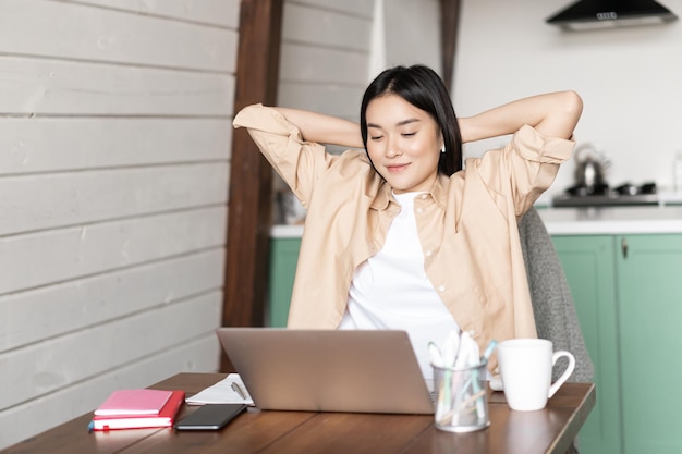 Immagine di una ragazza asiatica sorridente che finisce i compiti o lavora al computer portatile che sembra soddisfatta del risultato sul computer ...