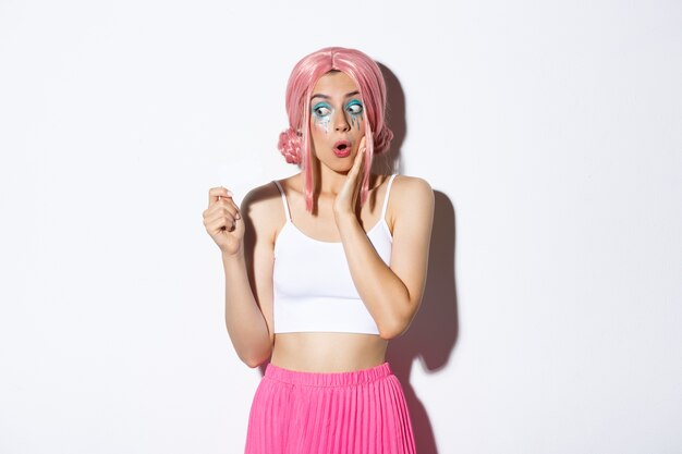 Immagine di una ragazza sciocca eccitata con parrucca anime rosa e trucco luminoso, guardando stupito dalla carta di credito, facendo shopping per le vacanze, in piedi.