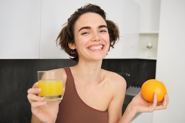 Immagine di una ragazza sportiva che tiene in mano un bicchiere di succo e un'arancia che beve vitamina beve sorridente