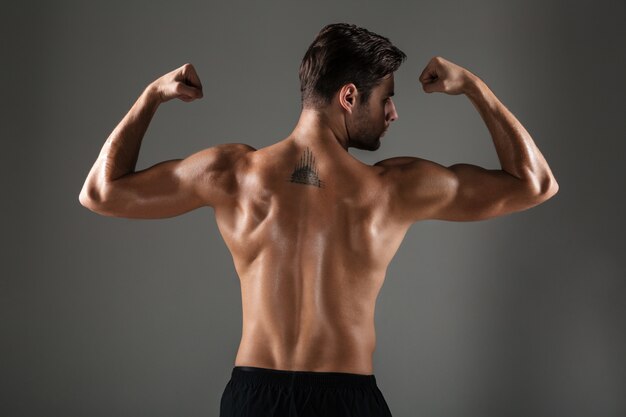 Immagine di vista posteriore di giovane uomo di sport che mostra il bicipite