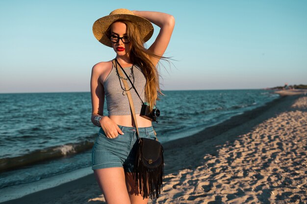 Immagine estiva all'aperto di bella donna bionda in cappello di paglia che cammina vicino al mare.