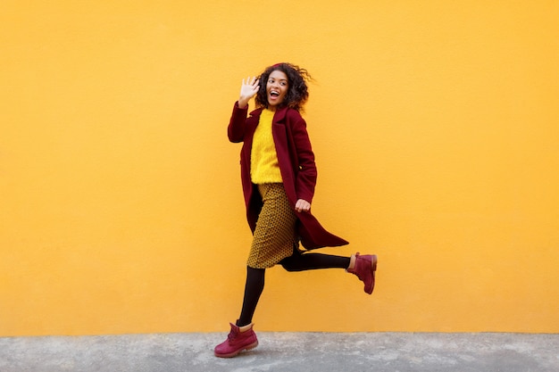 Immagine integrale della donna eccitata che salta con l'espressione del viso felice sul giallo.