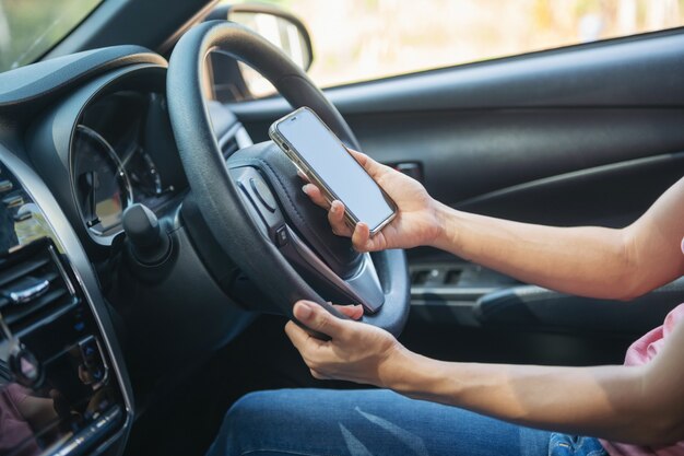 Immagine mockup di una donna che tiene e usa il telefono cellulare con schermo vuoto mentre guida un'auto, per GPS, foto di stili di vita in auto, interni, vista frontale. Con il telefono della tenuta della mano della donna.