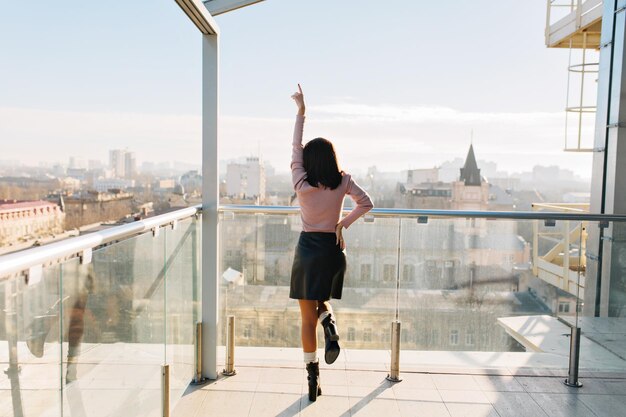 Immagine moderna ed elegante della città di una giovane donna attraente che si diverte sulla terrazza al mattino soleggiato. Vita da grande città, grande successo, affari, felicità, buona fortuna, positività