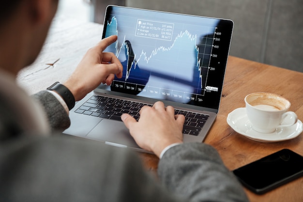 Immagine potata dell'uomo d'affari che si siede dalla tavola in caffè e che analizza gli indicatori sul computer portatile