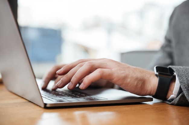 Immagine potata dell'uomo d'affari che si siede dalla tavola in caffè e che utilizza computer portatile