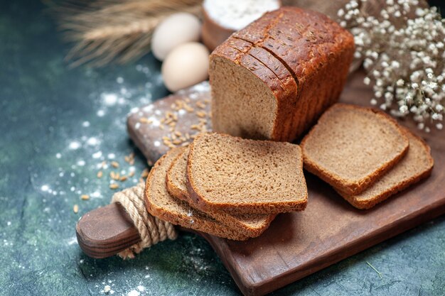 Immagine ravvicinata di frumenti dietetici di pane nero su tagliere di legno picchi di farina di uova di fiori in una ciotola su sfondo blu