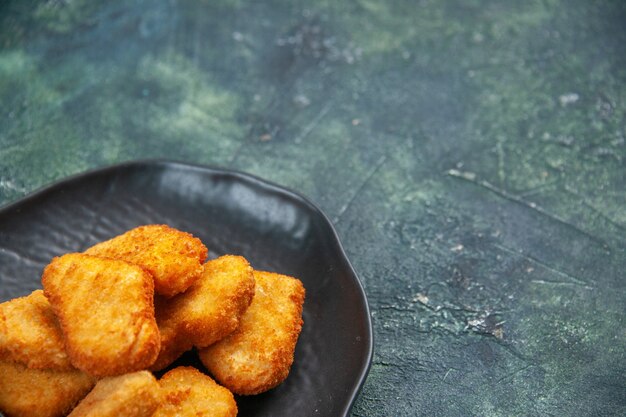 Immagine ravvicinata di gustose pepite di pollo in piastra nera su superficie scura con spazio libero