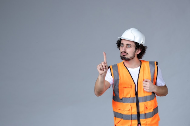 Immagine ravvicinata di un architetto maschio nervoso in giubbotto di avvertimento con casco di sicurezza e rivolto verso l'alto sopra la parete grigia dell'onda