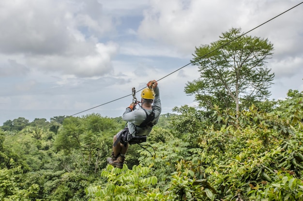 Immagine ravvicinata di un uomo appeso e scorrevole sulla zipline in un bellissimo parco con cielo nuvoloso