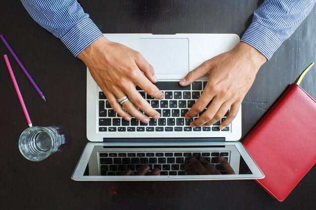 Immagine ritagliata di un giovane che lavora sul suo laptop a casa vista dall'alto delle mani dell'uomo d'affari impegnate nell'uso del laptop alla scrivania dell'ufficio