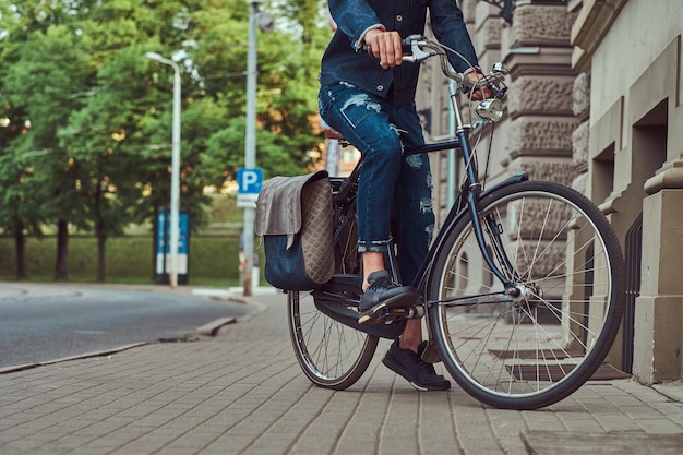 Immagine ritagliata di un uomo alla moda in abiti eleganti in sella a una bicicletta da città.