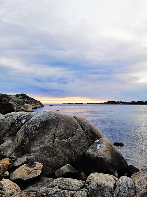 Immagine verticale del mare circondato da rocce sotto un cielo nuvoloso durante il tramonto in Norvegia