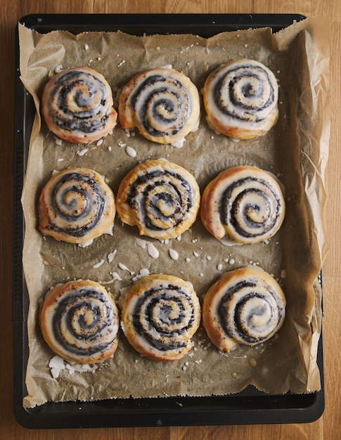 Immagine verticale di deliziosi pasticcini di lumache di papavero con una glassa di zucchero in un vassoio sul tavolo di legno