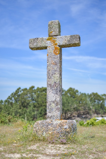 Immagine verticale di una croce di pietra ricoperta di muschi immersa nel verde sotto la luce del sole