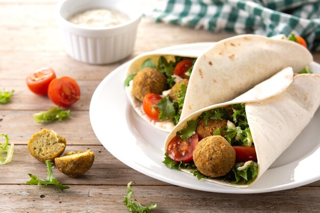 Impacco di tortilla con falafel e verdure su tavola di legno