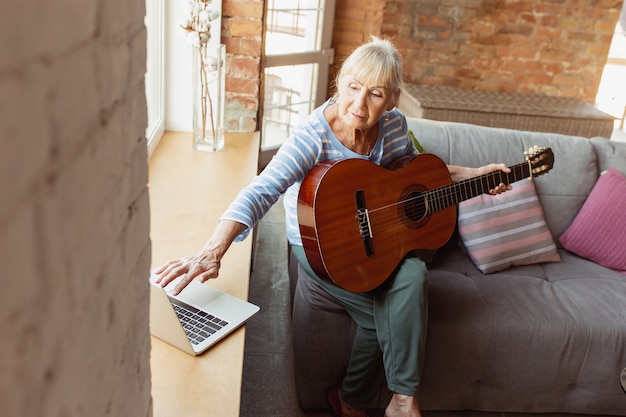 Imparare a suonare la chitarra online. Donna anziana che studia a casa, riceve corsi online