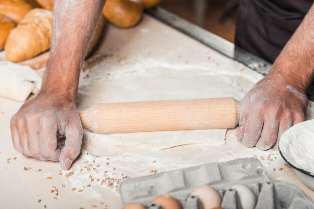 Impasto per appiattire la mano del fornaio maschio con mattarello