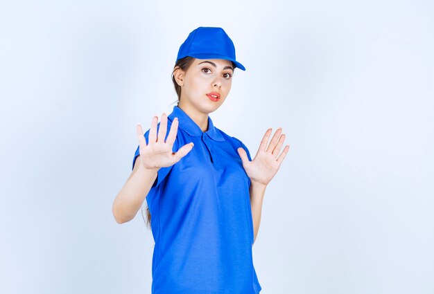 Impiegata della donna delle consegne in uniforme blu in piedi e che mostra il segnale di stop.