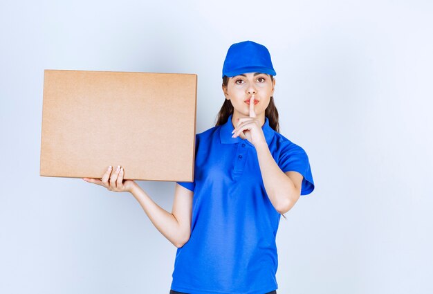 Impiegata della donna di consegna con la scatola di carta del mestiere che mostra il segno silenzioso.