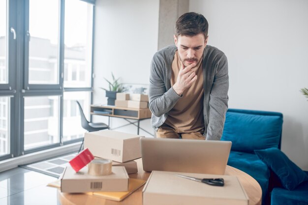 Impiegato concentrato del negozio di Internet che fissa lo schermo del suo laptop